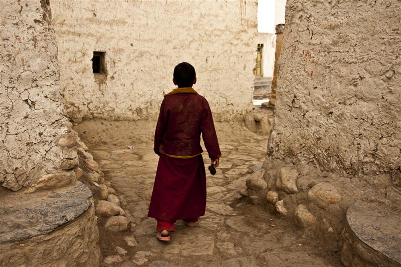 A youg monk in red robes walks in the walled city of Lo Manthang.